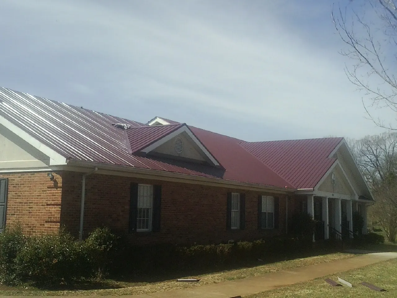 Red metal roof with gabled entries on a long brick building, from a Hail Damage Roof Repair job in Norwood