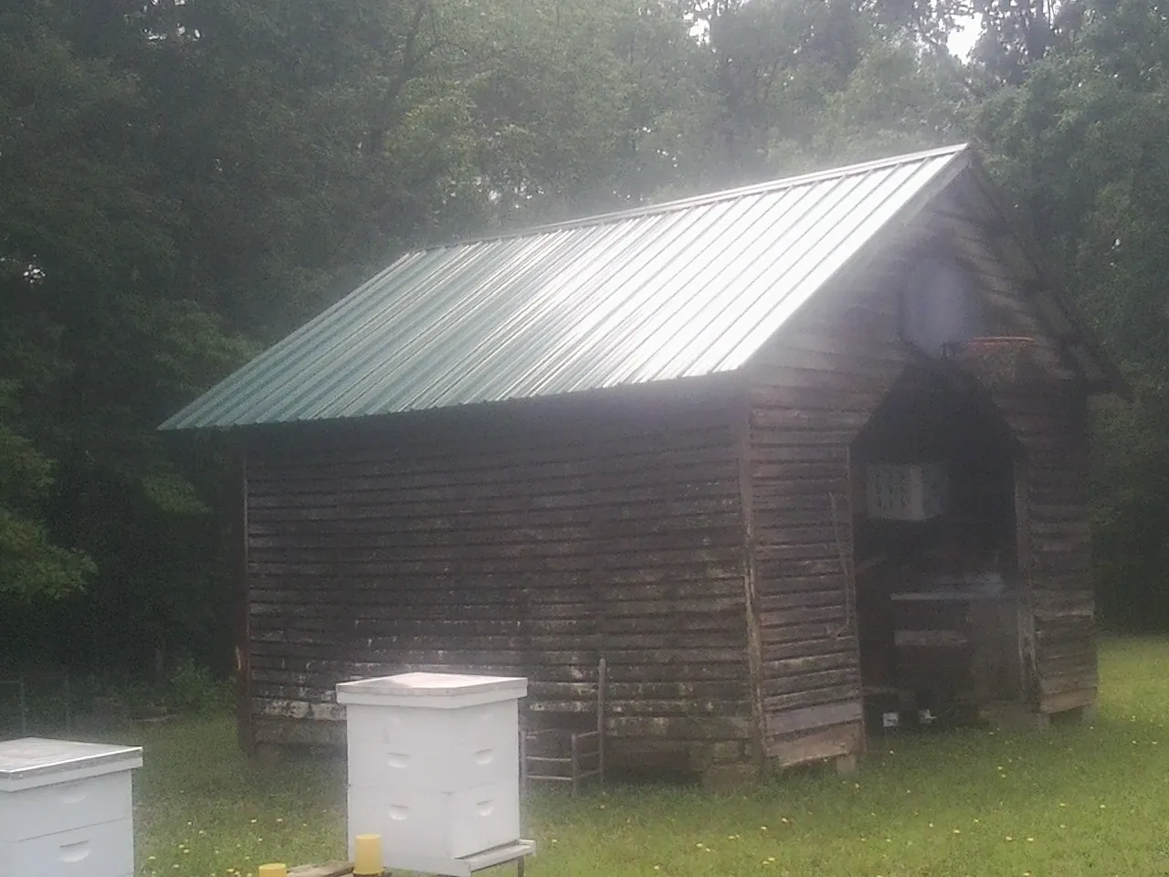 Green metal roof on a weathered barn beside stacked beehives in Norwood