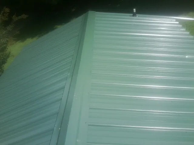 New green metal panels meeting at the ridge of a roof — Flat Roof Repair work by our crew in Norwood